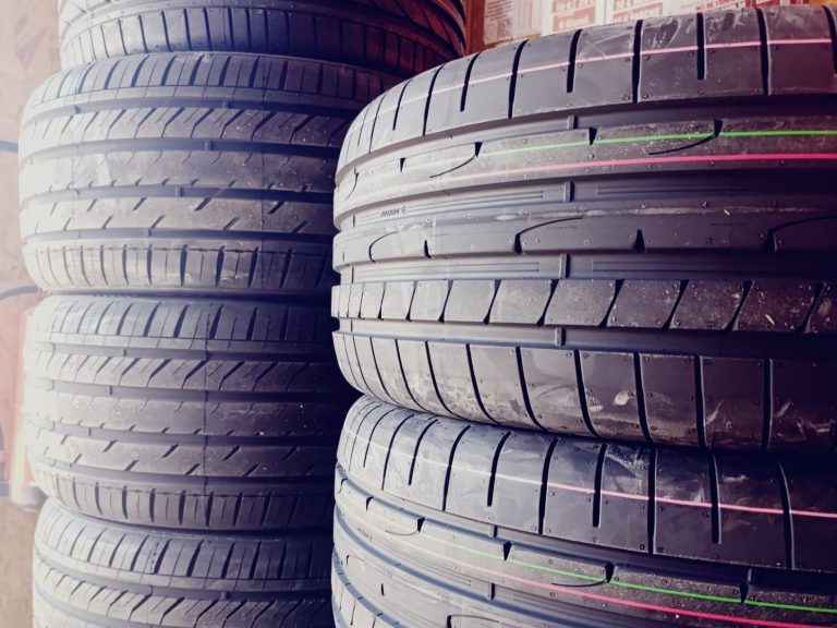 Coche gris aparcado cerca de un neumático de alto rendimiento con etiqueta visible.